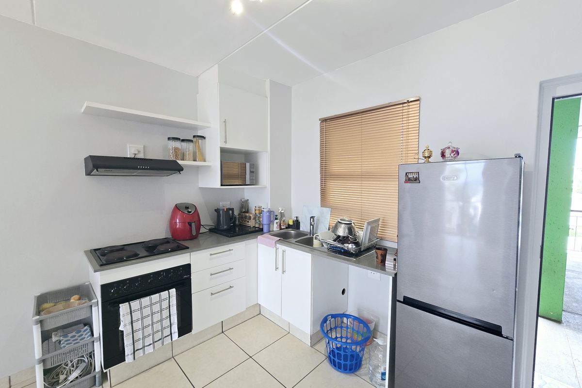 Compact kitchen featuring white cabinetry, electric hob, built-in oven, extractor fan, and tiled flooring, with a functional layout and stainless steel sink.