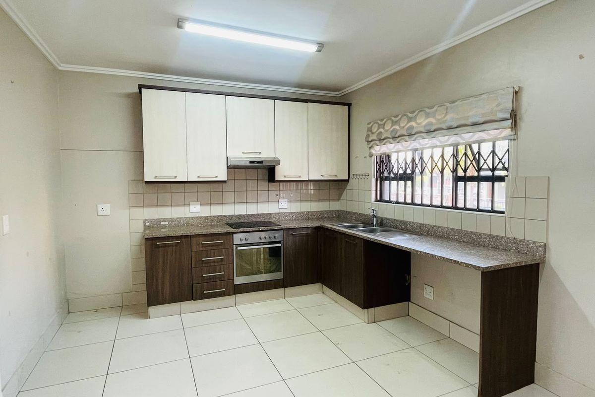 A functional kitchen featuring two-tone cabinetry, granite countertops, integrated oven and hob, and tiled flooring with a secure window.