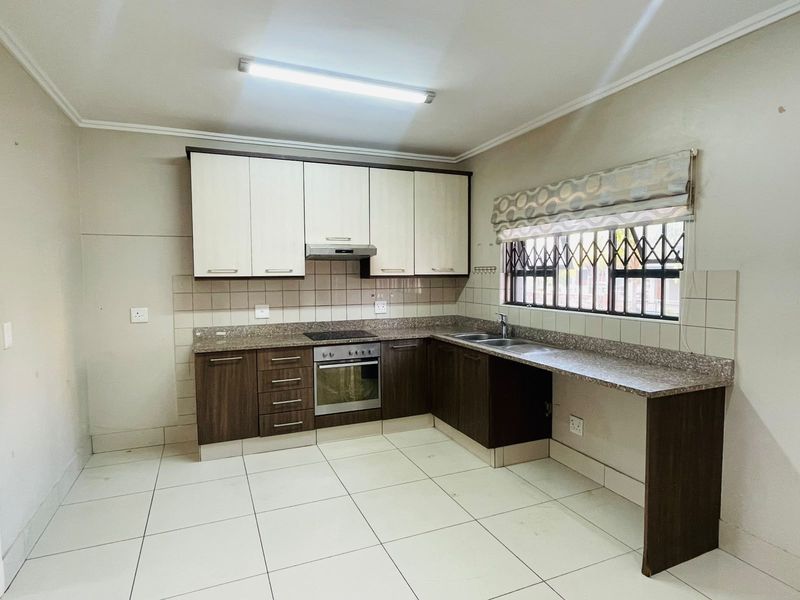 A functional kitchen featuring two-tone cabinetry, granite countertops, integrated oven and hob, and tiled flooring with a secure window.