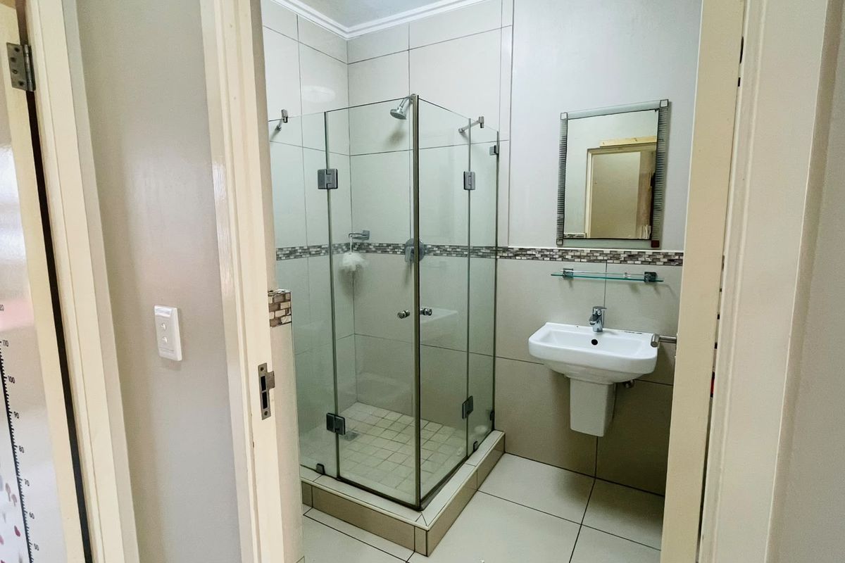 A clean and functional bathroom featuring a glass-enclosed shower, pedestal basin, and neutral ceramic tiling throughout.