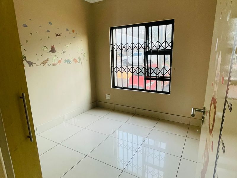 A bright, empty bedroom featuring tiled flooring, a built-in cupboard, and a window fitted with a security gate.