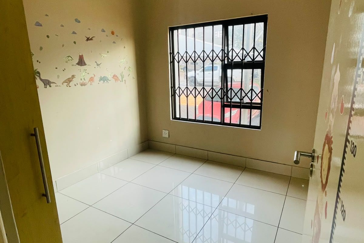 A bright, empty bedroom featuring tiled flooring, a built-in cupboard, and a window fitted with a security gate.