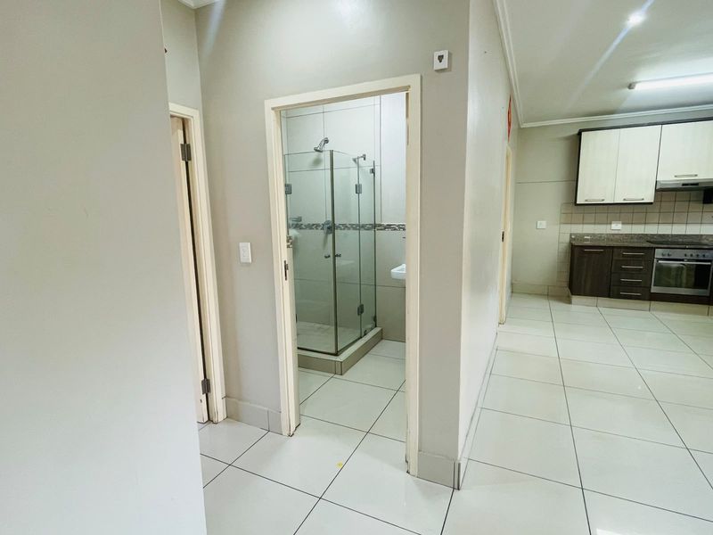 Open plan apartment interior featuring tiled flooring, a modern kitchen with built-in cabinetry and appliances, and access to a bathroom with a glass shower.