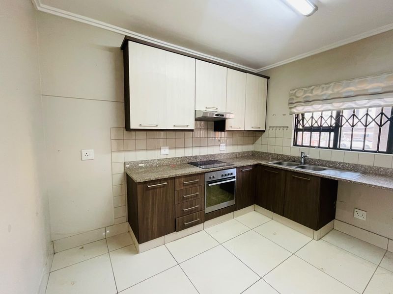 A functional kitchen featuring two-tone cabinetry, stone countertops, integrated oven and hob, and tiled flooring with a window fitted with security bars.