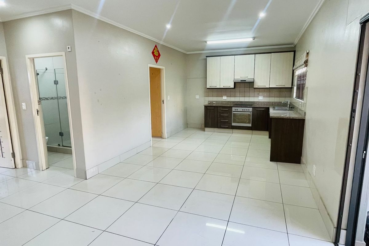 Open plan living area featuring a functional kitchen with built-in cabinetry, granite countertops, and tiled flooring, adjacent to a bathroom with a glass shower.