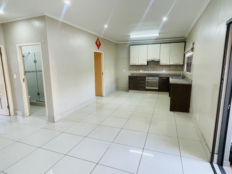 Open plan living area featuring a functional kitchen with built-in cabinetry, granite countertops, and tiled flooring, adjacent to a bathroom with a glass shower.