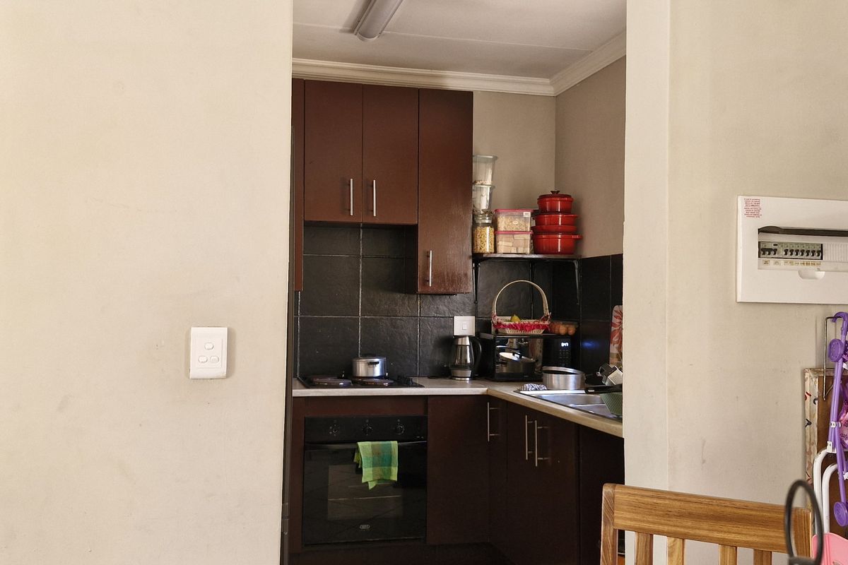 Compact kitchen featuring dark wood cabinetry, tiled backsplash, built-in oven and hob, and a functional sink area.