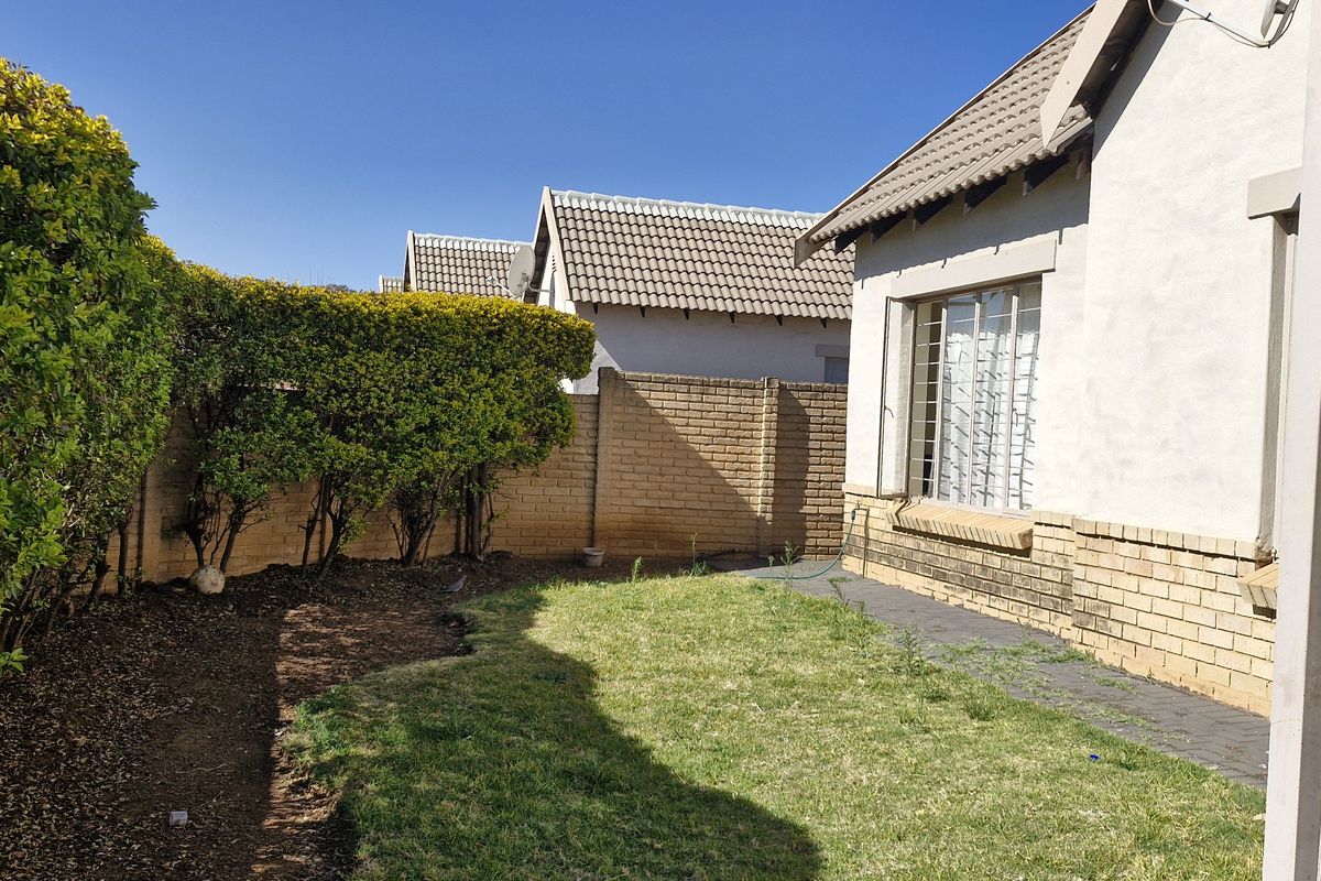 A rear garden area featuring a small lawn, paved walkway, and brick boundary wall with established hedging.