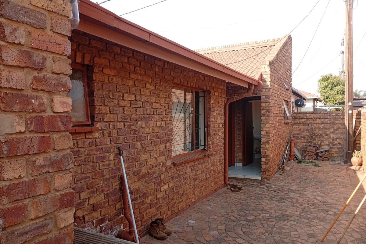 A rear exterior view of a face brick house featuring a paved courtyard area and traditional tiled roofing.