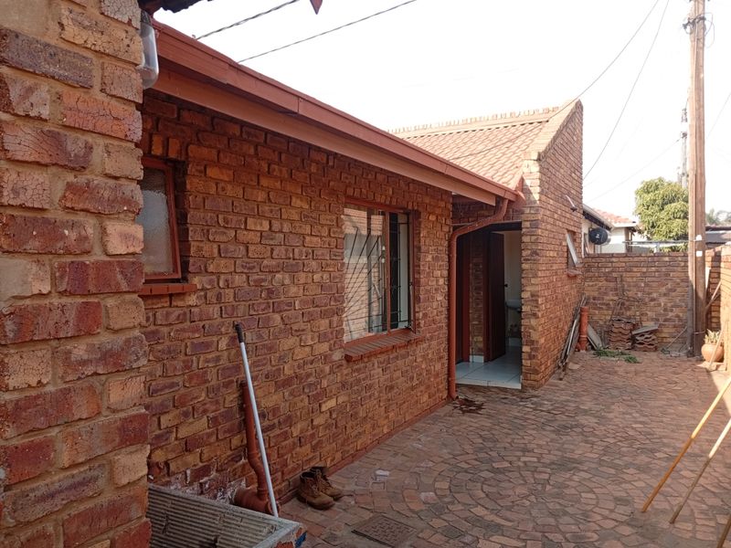 A rear exterior view of a face brick house featuring a paved courtyard area and traditional tiled roofing.
