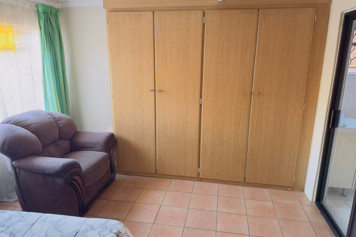 A bedroom featuring built-in wooden cupboards and tiled flooring, with access to an adjacent area through a sliding door.