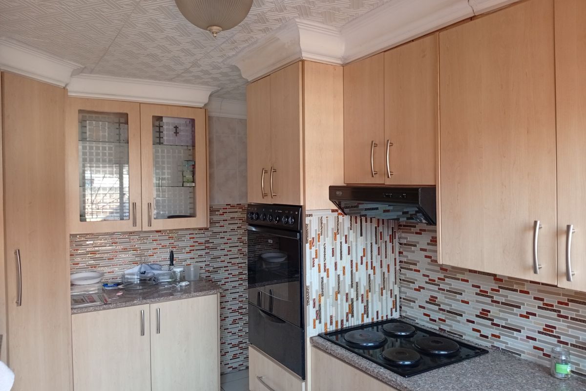A functional kitchen featuring light wood-tone cabinetry, mosaic tile backsplash, built-in oven, and electric hob with an integrated extractor fan.