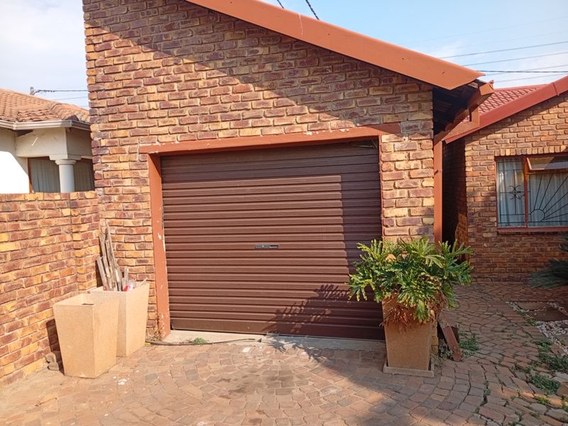 A single-car garage featuring a brown roll-up door, set within a face-brick exterior and complemented by a paved driveway area.