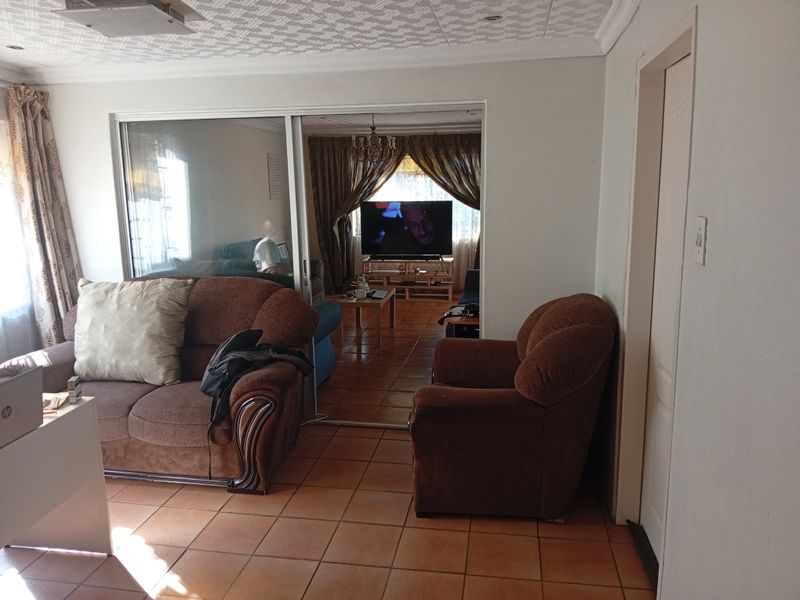 A living room area featuring tiled flooring, a textured ceiling, and a sliding glass door leading to an adjacent lounge space.