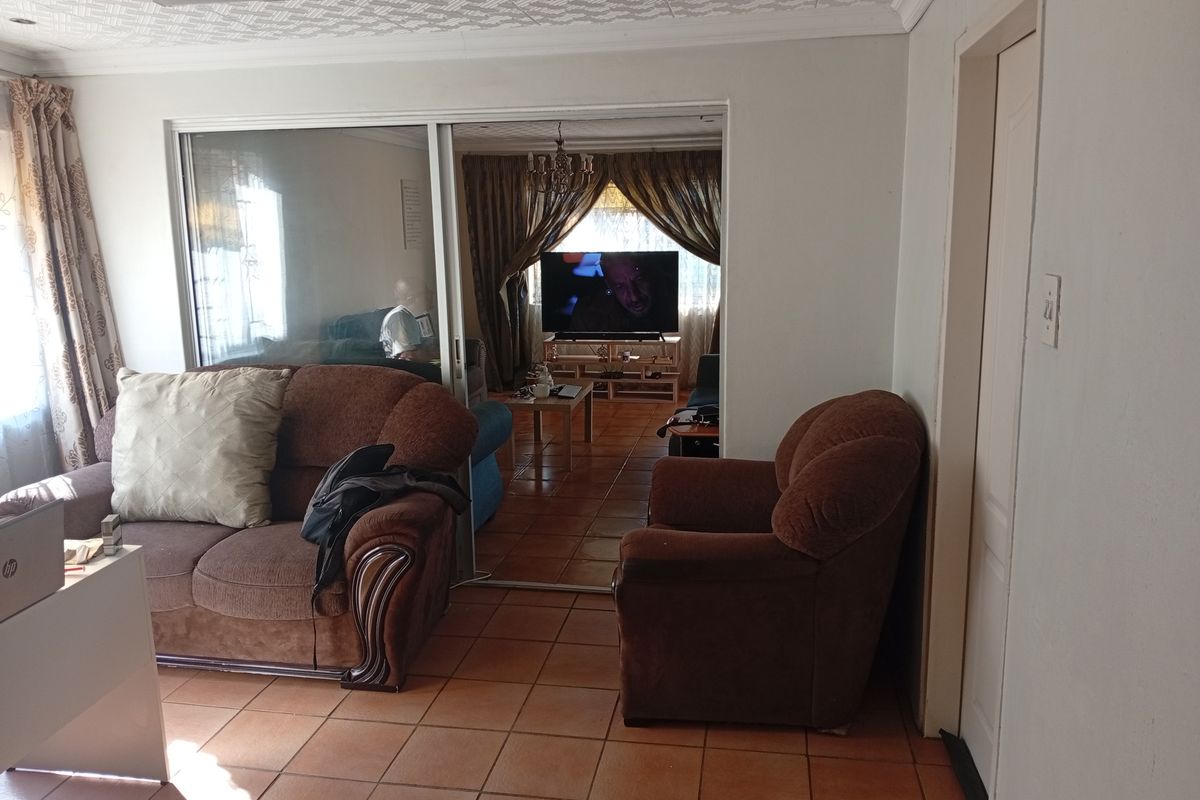 A living room area featuring tiled flooring, a textured ceiling, and a sliding glass door leading to an adjacent lounge space.