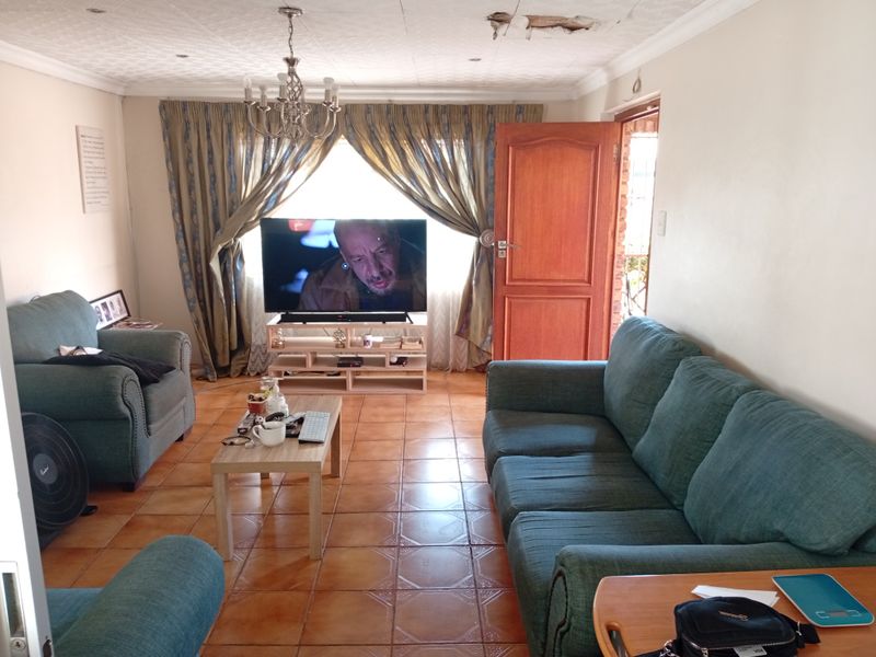 A living room featuring tiled flooring, a chandelier, and a timber door, currently showing visible damage to the ceiling plaster.
