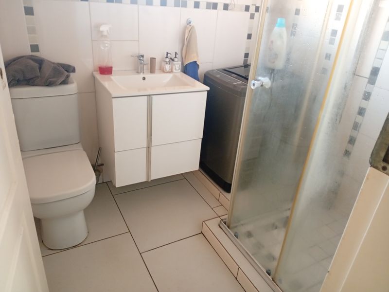 A functional bathroom featuring a white vanity, toilet, and a glass-enclosed shower with tiled walls and flooring.