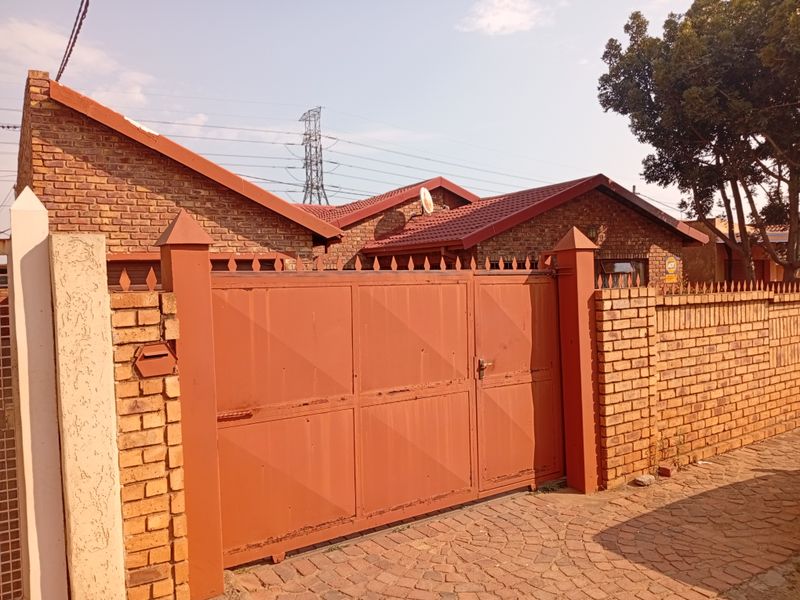 Front view of a face brick house featuring a secure metal driveway gate and paved entrance area.