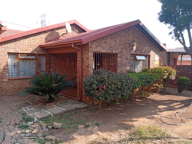 A front view of a face brick house featuring a tiled roof, security gates, and a paved entrance path with established garden shrubs.