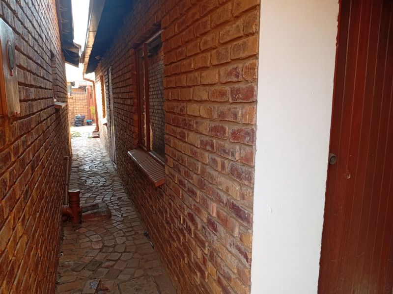 A narrow side passage featuring exposed brick walls, cobblestone paving, and access to the rear of the property.