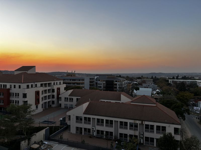 Aerial view of a residential apartment complex featuring tiled roofs, paved courtyards, and surrounding urban landscape during sunset.