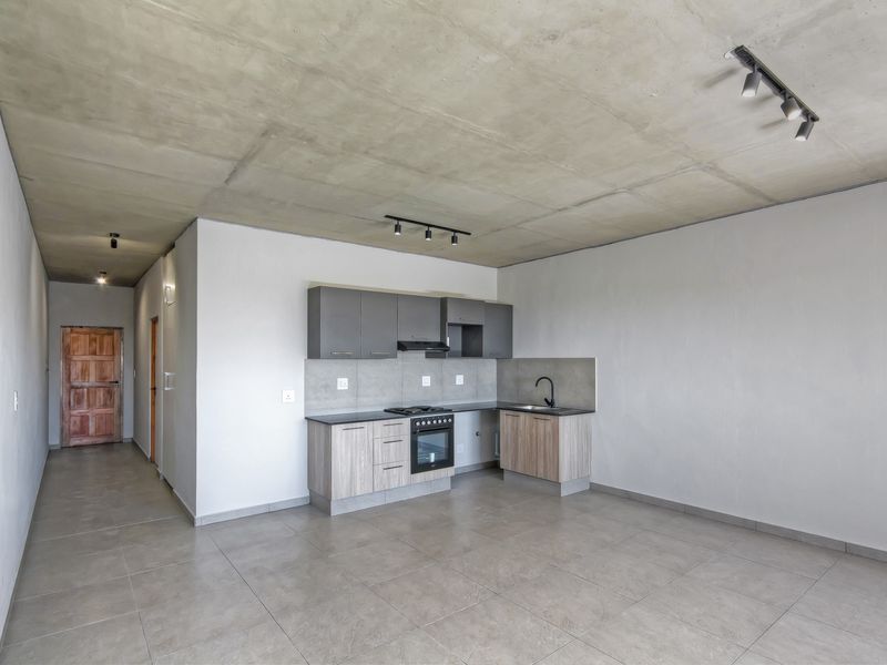 Modern open-plan kitchen featuring exposed concrete ceilings, sleek cabinetry, built-in appliances, and neutral tiled flooring in a spacious, minimalist apartment setting.