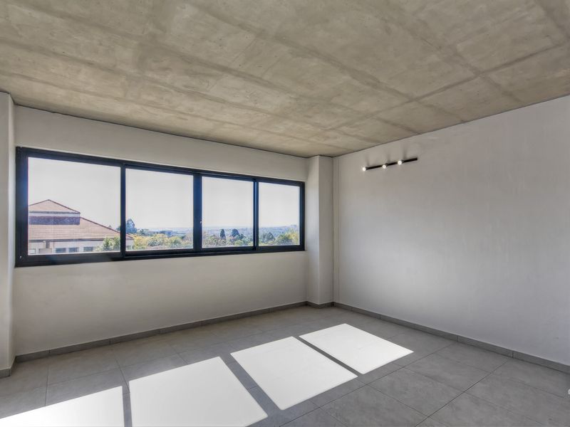 A bright, modern bedroom featuring an exposed concrete ceiling, large windows with scenic views, and neutral tiled flooring.