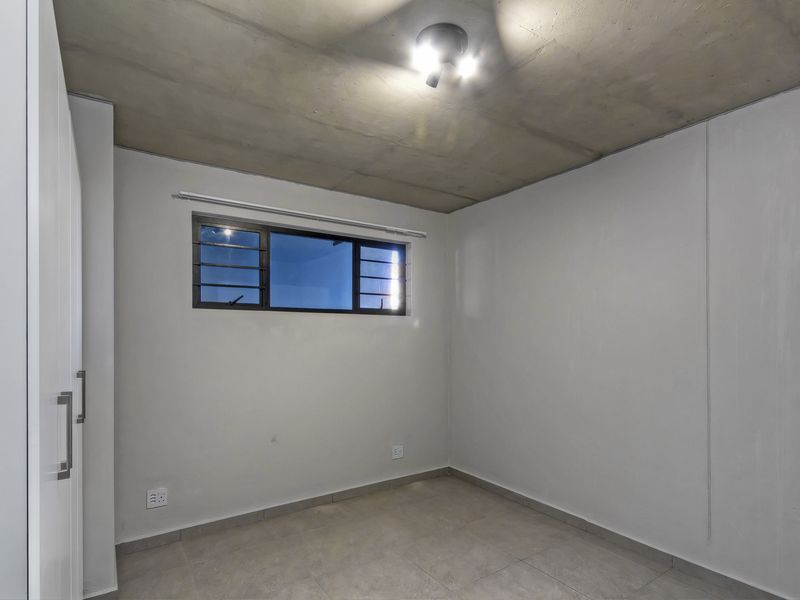 An empty bedroom featuring tiled flooring, a built-in wardrobe, and an exposed concrete ceiling, providing a neutral canvas for personalization.