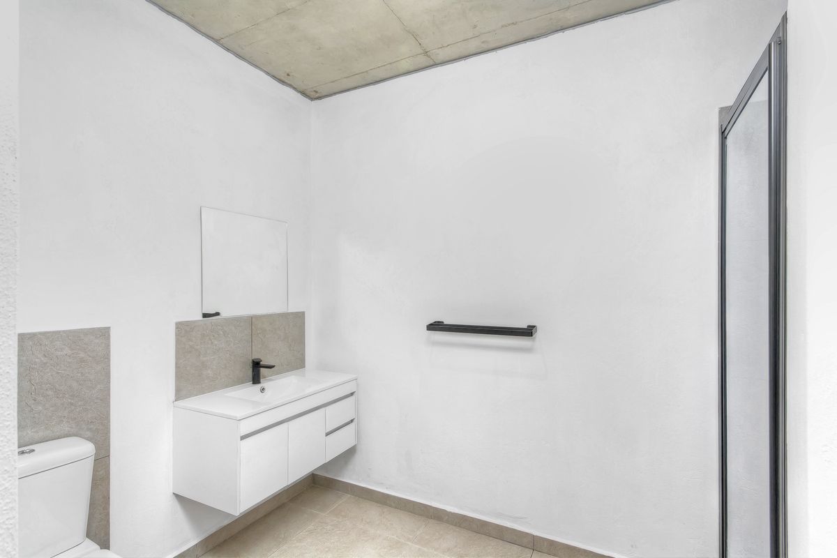 A modern, minimalist bathroom featuring a wall-mounted vanity, black fixtures, a shower enclosure, and an exposed concrete ceiling.