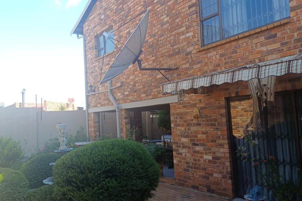 Rear view of a face brick house featuring a paved patio area, retractable awning, and satellite dish installation.