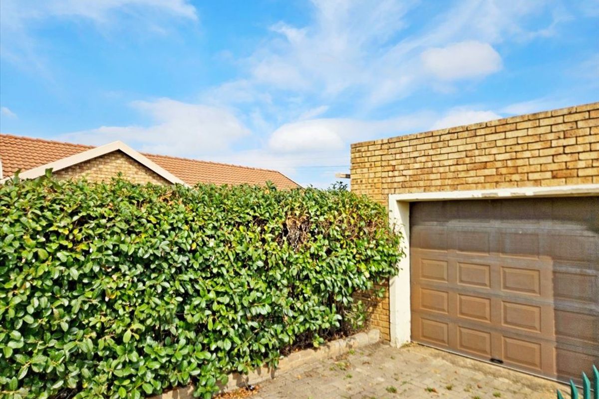 Exterior view of a townhouse garage featuring a sectional door, brick masonry, and a paved driveway area bordered by a mature hedge.