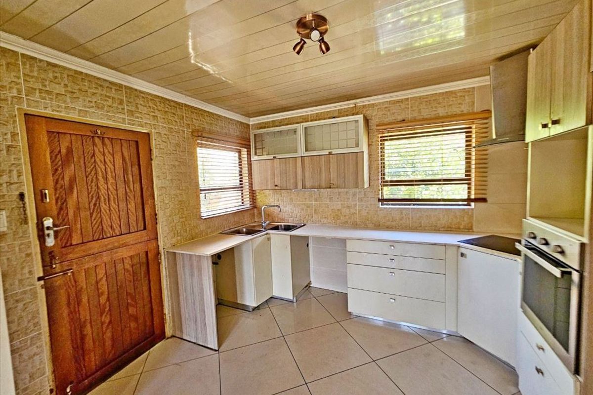 A functional kitchen featuring built-in cabinetry, a stainless steel sink, integrated oven, extractor fan, and tiled finishes throughout.