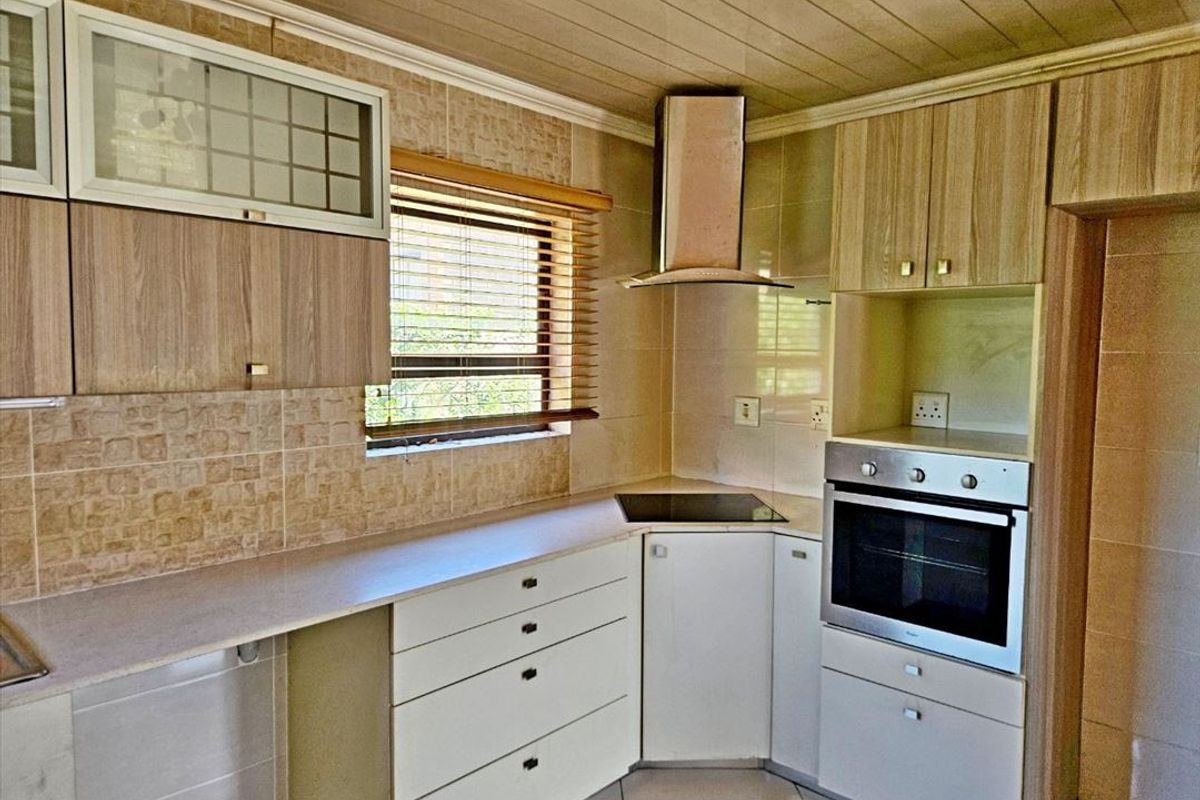 A functional kitchen featuring built-in cabinetry, a stainless steel extractor fan, integrated oven, and tiled splashbacks with a timber-paneled ceiling.