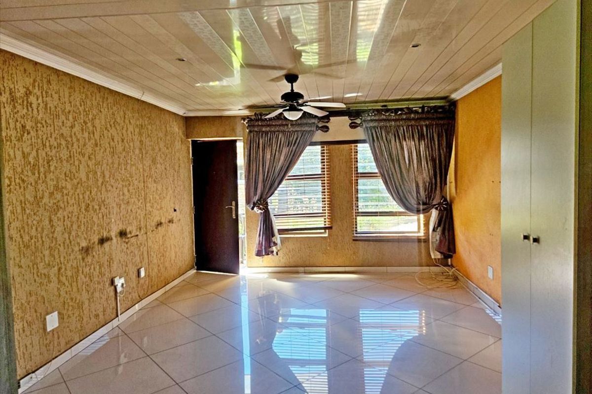 An empty living room featuring tiled floors, a ceiling fan, and built-in storage, requiring cosmetic updates to the wall finishes.