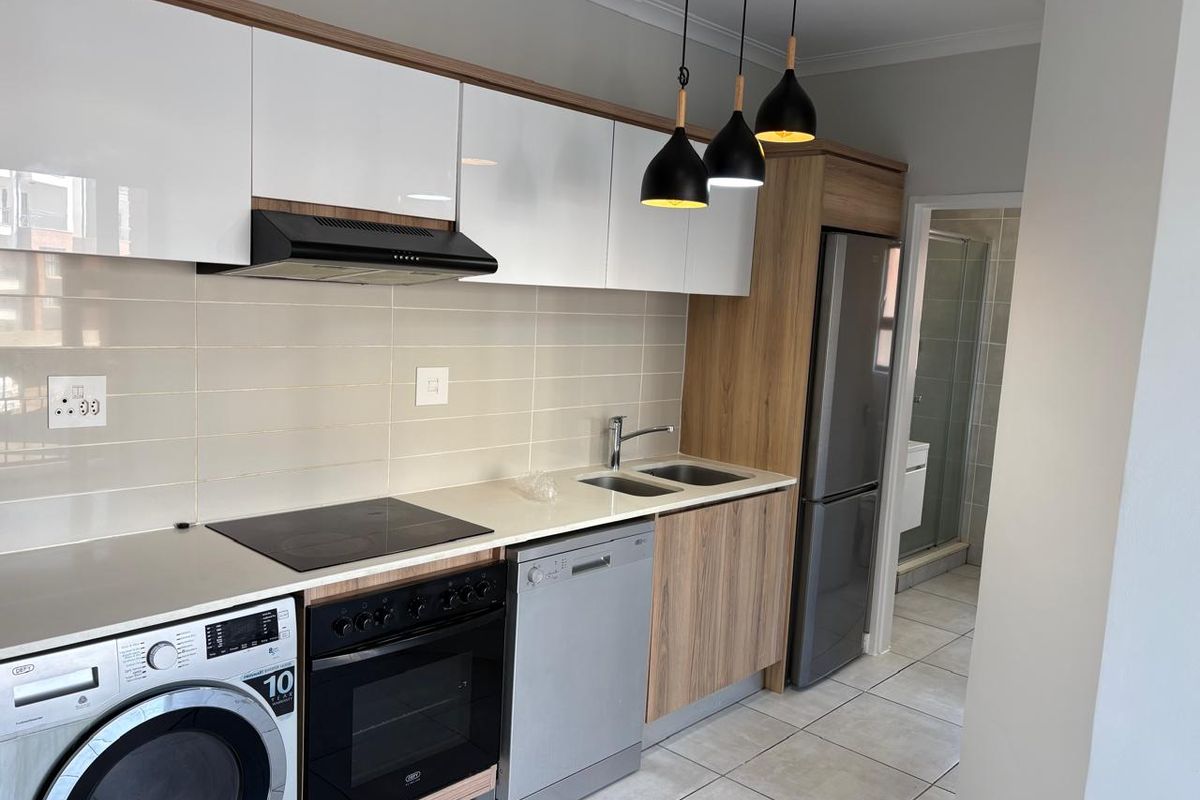 Modern kitchen featuring sleek white and wood-grain cabinetry, integrated appliances, electric hob, oven, and tiled backsplash with contemporary pendant lighting.