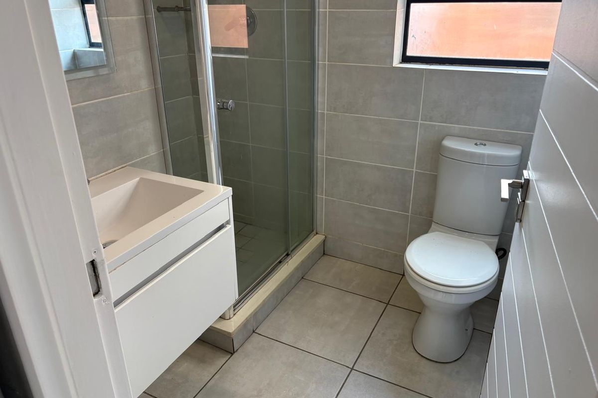 A clean, modern bathroom featuring a glass shower enclosure, a wall-mounted vanity basin, and a standard toilet with neutral grey wall and floor tiles.