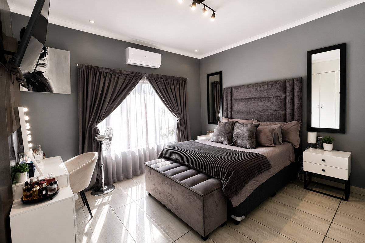 A well-maintained bedroom featuring tiled flooring, modern track lighting, a wall-mounted air conditioning unit, and neutral grey wall finishes.