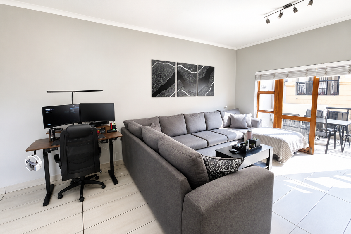 A bright and modern living room featuring large format floor tiles, track lighting, and a sliding glass door providing access to an outdoor balcony area.