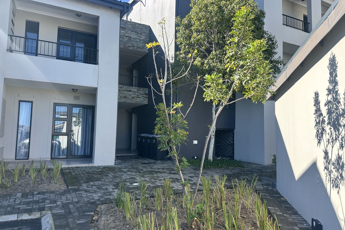 A view of the apartment building's rear courtyard featuring paved ground, stone-clad accents, and balconies with metal railings.