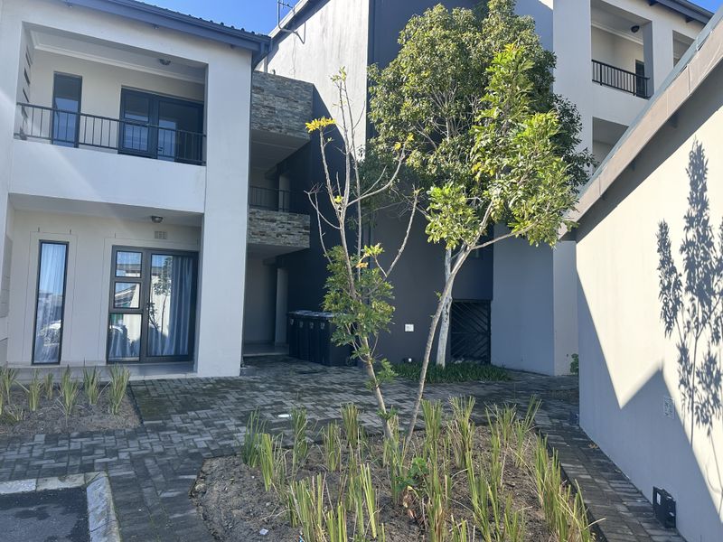 A view of the apartment building's rear courtyard featuring paved ground, stone-clad accents, and balconies with metal railings.