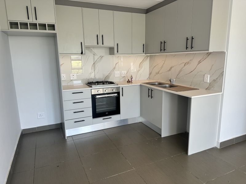 Modern kitchen featuring light grey cabinetry, stone countertops, marble-look splashback, gas hob, electric oven, and tiled flooring in a clean, contemporary finish.