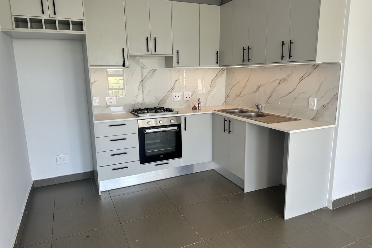 Modern kitchen featuring light grey cabinetry, stone countertops, marble-look splashback, gas hob, electric oven, and tiled flooring in a clean, contemporary finish.
