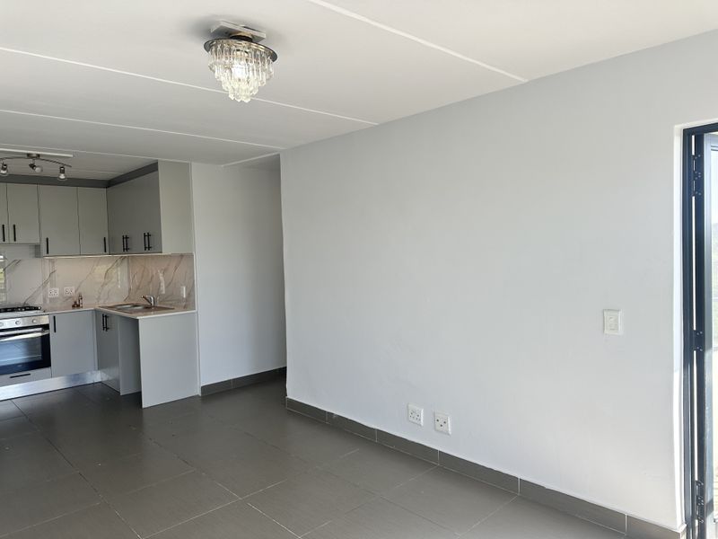 Modern open-plan living area featuring a sleek kitchen with built-in cabinetry, integrated appliances, and neutral tiled flooring throughout.