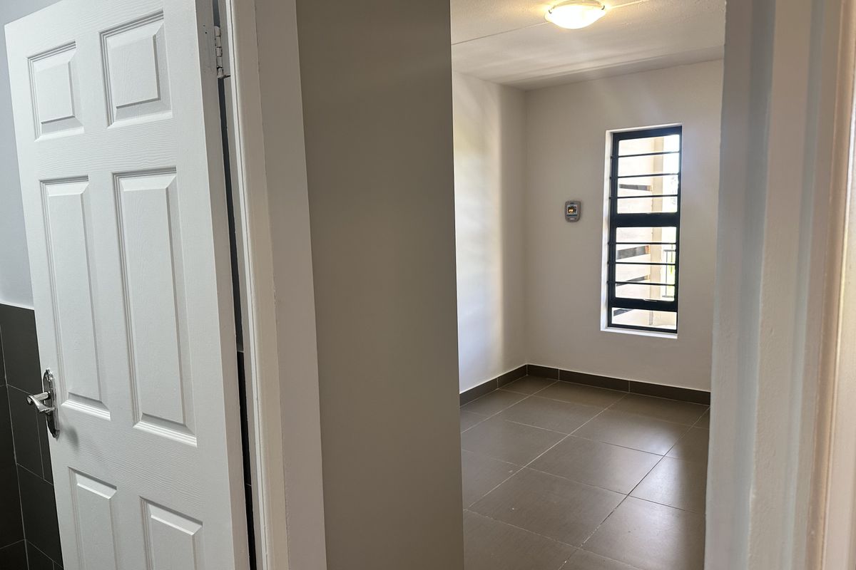 A clean, empty bedroom featuring neutral tiled flooring, a window with security bars, and a simple ceiling light fixture.