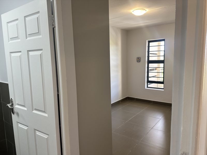 A clean, empty bedroom featuring neutral tiled flooring, a window with security bars, and a simple ceiling light fixture.