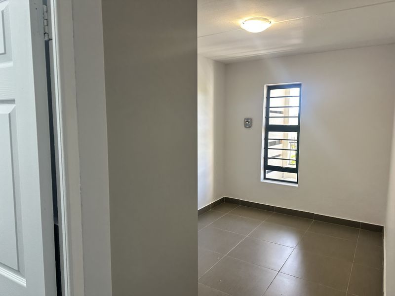 A clean, empty bedroom featuring neutral tiled flooring, a window with security bars, and a simple ceiling light fixture.