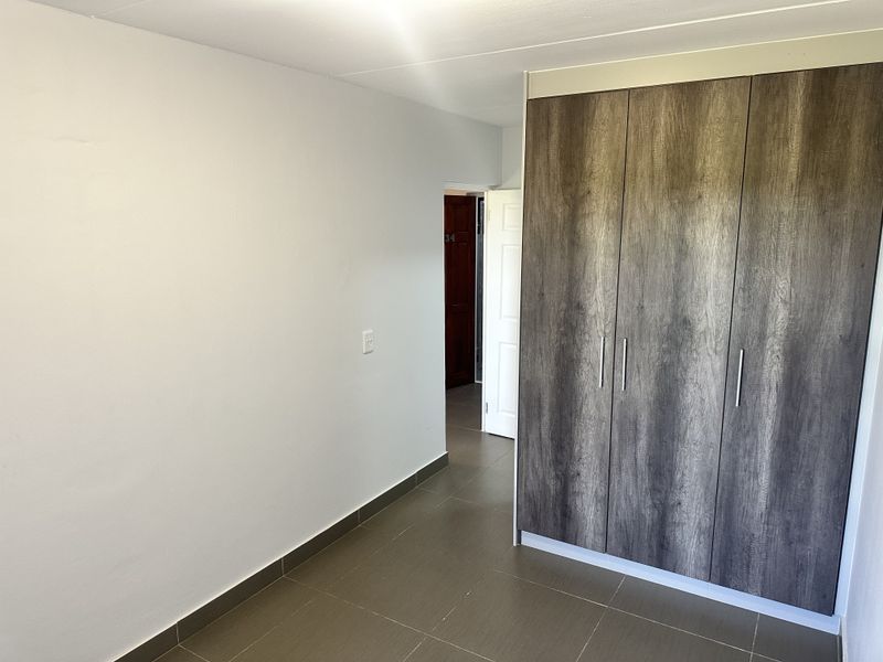 A clean, empty bedroom featuring modern wood-look built-in cupboards and neutral tiled flooring, offering a versatile space ready for personalization.