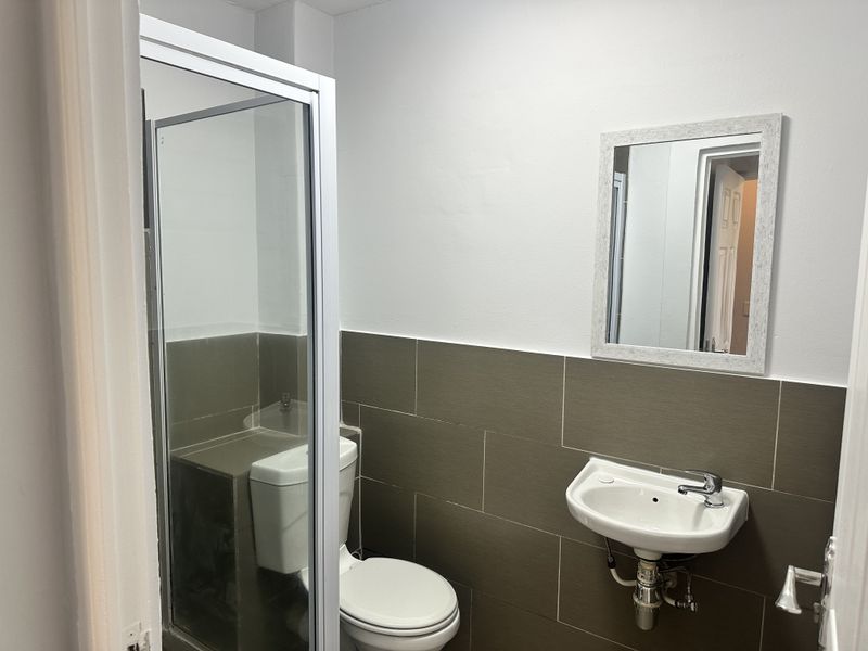 A functional bathroom featuring a shower enclosure, wall-mounted basin, and neutral tiled wall finishes.