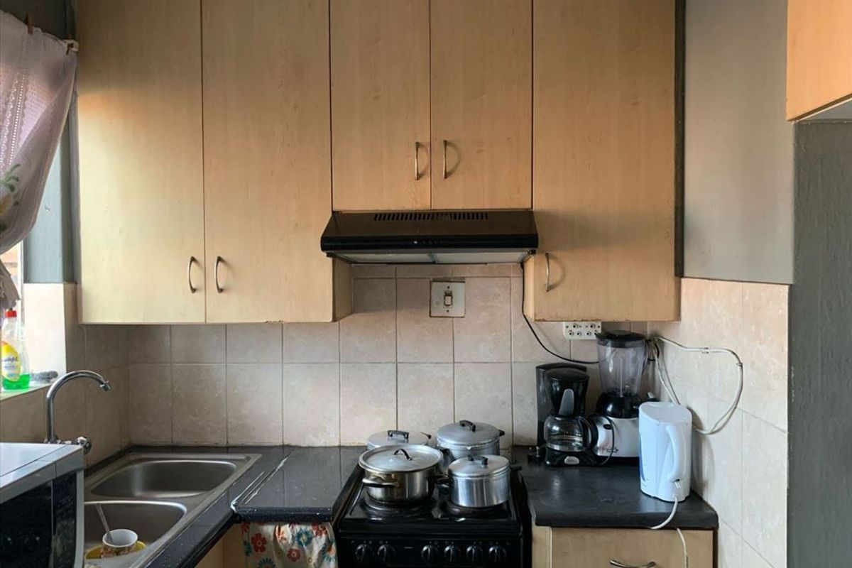 A compact kitchen featuring laminate cabinetry, a black stone countertop, double bowl sink, and a built-in extractor fan with tiled backsplash.