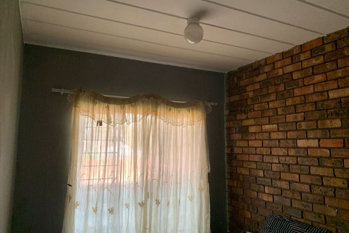 A bedroom featuring a rustic exposed brick feature wall and a white tongue and groove ceiling.